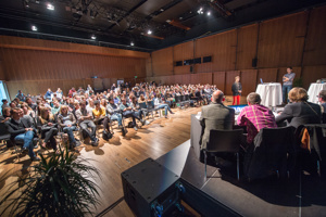 Vortragsteilnehmer:innen in Reihenbestuhlung, Bühne mit Stehtischen und Podium im Seestudio im Festspielhaus Bregenz