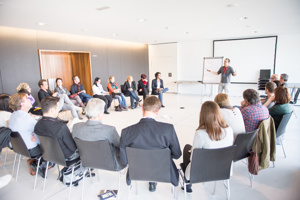 Workshopteilnehmer:innen in einem Stuhlkreis und einem Vortragenden mit Flipchart und Leinwand in der weißen Seegalerie