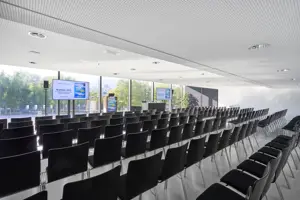 © Anja Koehler Schwarze Stuhlreihen vor zwei Großbildschirmen im weißen Saal Bodensee im Festspielhaus Bregenz mit Blick auf den Vorplatz © Anja Koehler