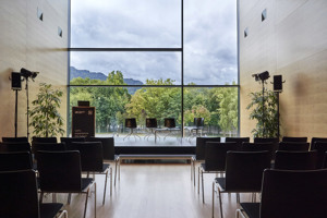 Saal Propter Homines mit Blick ins Grüne, Bühne und schwarze Stuhlreihen