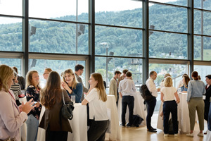 Kongressteilnehmer:innen stehen vergnügt an Stehtischen im Seefoyer vor der Glasfront mit Blick auf den begrünten Pfänder