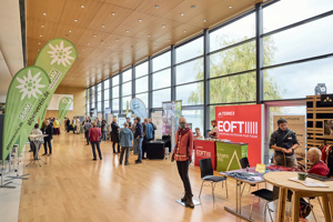 Tagungsteilnehmer:innen in der Fachausstellung im Seefoyer im Festspielhaus Bregenz mit Bick auf den Bodensee
